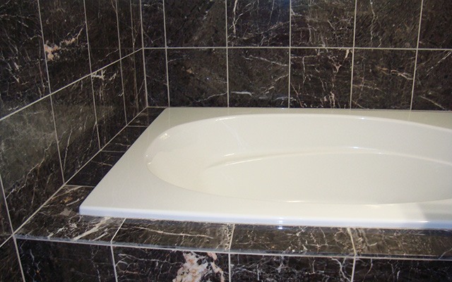 a white bath tub inside of a bathroom with black tiles