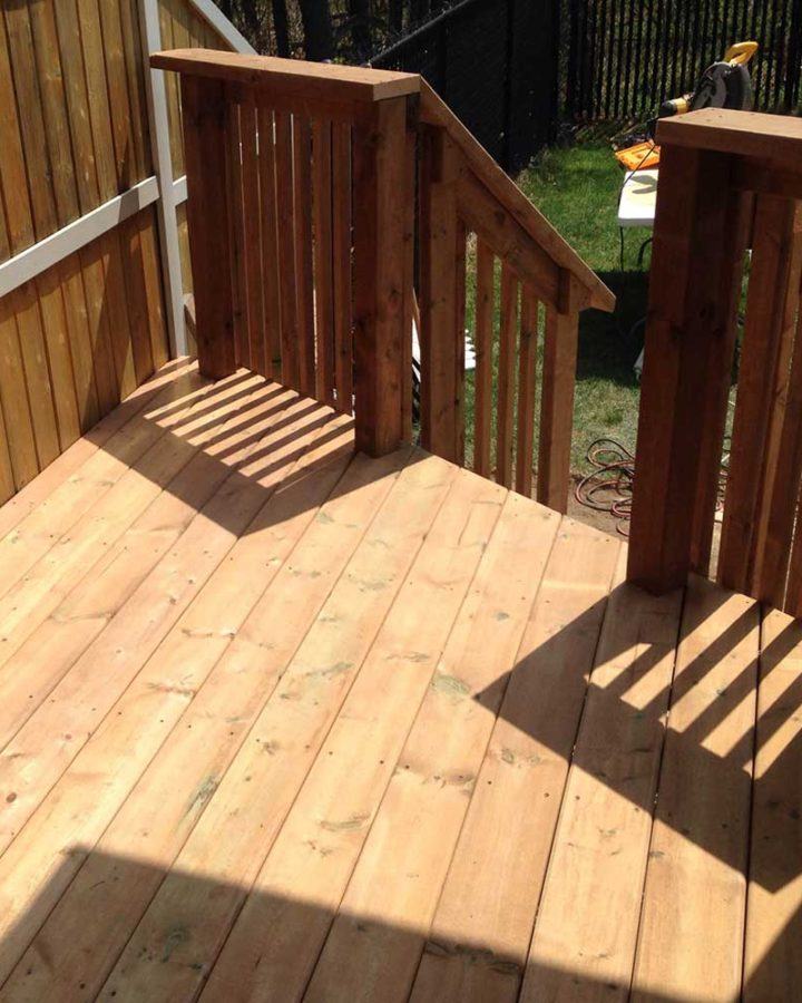 a wooden deck with railings and a fence in the background